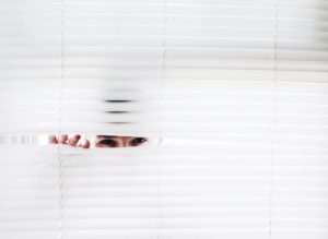 Person peeking through their window blinds in Glasgow.